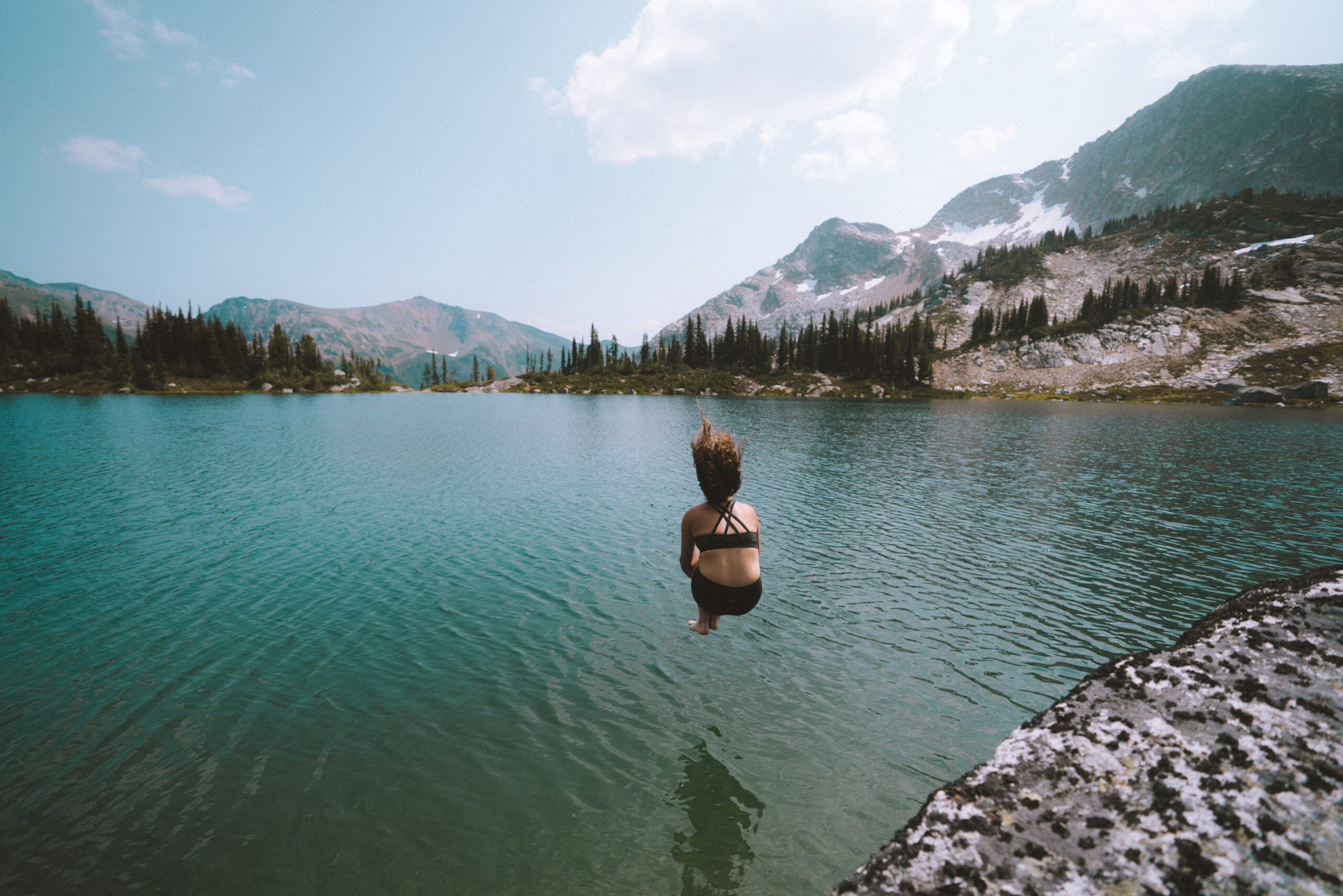 A woman cannonballs into a alpine lake at Whitecap Alpine.